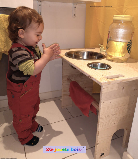 bebe de un an qui se lave les mains a la table de lavage montessori artisanale